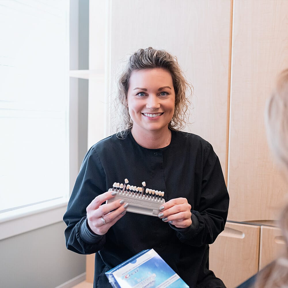 Dental hygienist showing patient shades of coloring at teeth whitening appointment