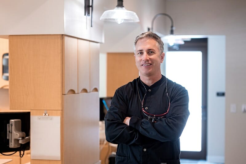 Dr. Batterton in hallway wearing black shirt and glasses around his neck