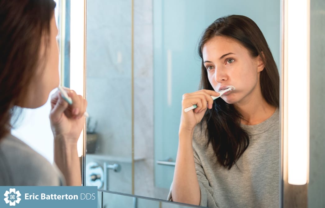 Woman brushing teeth in front of bathroom mirror